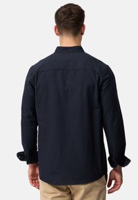 Camisa de manga larga azul marino de algodón, con cuello abotonado, canesú trasero y puños enrollados. Textura suave, ajuste relajado.