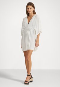 Vestido blanco con escote en V profundo, mangas cortas tipo kimono, cintura ceñida y falda fluida. Combinado con sandalias de plataforma negras con tirantes.