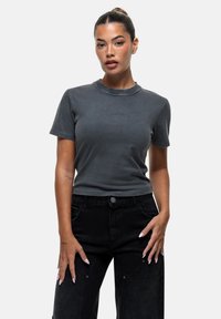 T-shirt grigia a maniche corte con scollo rotondo, design aderente e texture morbida, abbinata a jeans neri a vita alta con tasche.