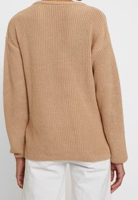 Beżowy sweter dziewiarski o luźnym kroju, prążkowanej fakturze i długich rękawach. Prosty design, okrągły dekolt i prosty dół z tyłu.