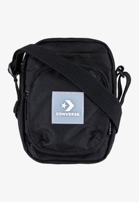 Borsa a tracolla nera con cinturino regolabile, tasca frontale con zip e patch in gomma grigio con design a stella e freccia. Materiale resistente.