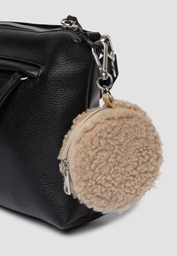 Schwarze, strukturiert gelegte Ledertasche mit einem beigefarbenen, runden, flauschigen Beutel, der mit einem silbernen Karabinerhaken und einem Reißverschluss befestigt ist.