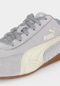 Κοντινό πλάνο ανοιχτόγκρι Puma σουέντ αθλητικού παπουτσιού με γκρι κορδόνια, λευκή λωρίδα λογότυπου και σόλα από καουτσούκ.