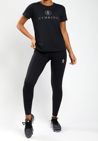 Černý sportovní top s logem "GYMKING", kombinovaný s přiléhavými černými legínami s drobným logem a texturovanými teniskami.