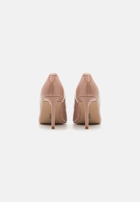 Scarpe col tacco alto in pelle verniciata color nudo con punte a punta e tacchi stiletto sinuosi, caratterizzate da una finitura liscia e lucida e da un design minimalista.
