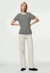 Μαύρη και λευκή ριγέ μπλούζα με στρογγυλή λαιμόκοψη, συνδυασμένη με εκρού παντελόνι με φαρδιά πόδια και μαύρα επίπεδα παπούτσια.