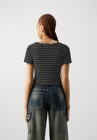 Černobíle pruhovaný krátký top se vroubkovaným výstřihem v kombinaci s volnými, vybledlými modrými širokými džíny s kapsami na cargo.