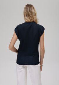 Mørkeblå kortermet topp med en løs passform. Stoffet er glatt og lett. Baksiden er ensfarget uten synlige mønstre eller detaljer.