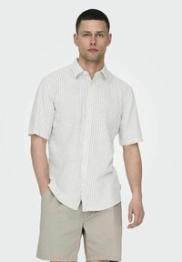 Korte ærmer knap-up skjorte i lys grå med hvide striber, der har klassisk krave og afslappet pasform. Bæres med beige shorts.