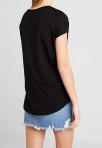 Svart kortärmad topp med rundad halsringning, med en mjukt böjd nederkant och slät textur, i kombination med slitna denimshorts.