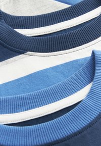 Nærbillede af tre stribede crew neck-trøjer i lag, med ribbede kraver i nuancer af blå, hvid og lysegråt stof.
