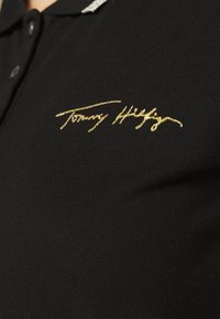 Sort polo skjorte med tekstureret stof, der har en guld broderet signatur og et sølv detaljer på kraven.