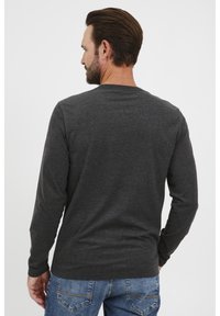Szürke, hosszú ujjú póló kerek nyakkivágással, texturált anyagból, slim fit szabású, kék farmernadrággal párosítva, hátulról nézve.