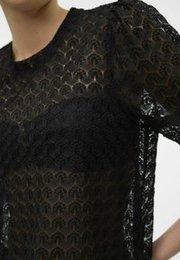 Top de encaje negro con patrones geométricos, mangas cortas abullonadas, cuello redondo y una textura transparente. Material suave y ligero.