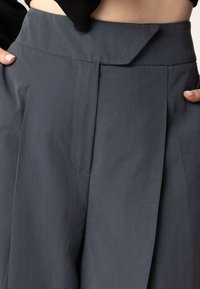 Donkergrijze broeken met een platte tailleband, voorzien van plooien aan de voorkant, minimale naden en een gladde, gestructureerde stof voor een gepolijste uitstraling.