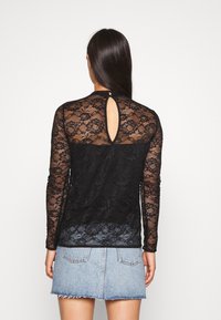 Top in pizzo nero a maniche lunghe con motivi floreali, design semitrasparente e chiusura a chiave sul retro. Abbinato a una gonna di jeans.