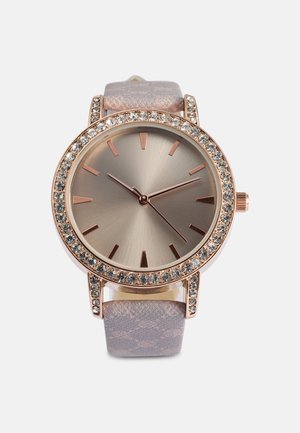 Montre en or rose avec un cadran rond, lunette ornée de cristaux et bracelets texturés taupe. Marqueurs d'heure et aiguilles minimalistes.