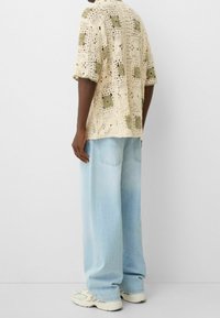 Camiseta de crochet color crema con patrones de cuadros verdes, combinada con jeans de pierna ancha azul claro y zapatillas crema. Diseño sencillo y texturizado.