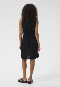 Schwarzes ärmelloses Kleid mit einem elastischen Bund, das einen lässigen Schnitt und einen knielangen Saum bietet. Kombiniert mit flachen schwarzen Sandalen.