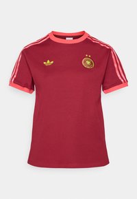 T-shirt à manches courtes bordeaux en coton. Présente des accents roses au niveau du col et des manches, ainsi qu'un logo Adidas jaune avec des étoiles et un emblème.