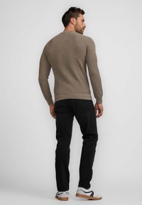 Beige knit sweater with long sleeves, paired with black jeans and white sneakers featuring black accents. Smooth texture; fitted design.