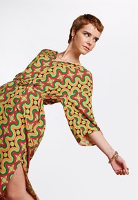 Vestito colorato con un motivo vorticoso di rosso, verde e giallo su un tessuto leggero, con maniche a tre quarti e uno spacco laterale.