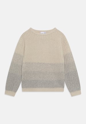 Chunky striktrøje med lange ærmer, rund hals og gradientfarver fra creme øverst til lysegrå nederst mod hvid baggrund.