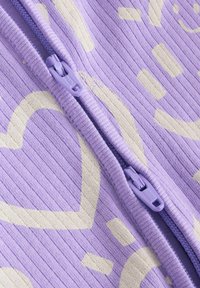 Vêtement zippé violet avec une texture côtelée. Présente des accents de cœur jaune clair et un motif le long de l'avant, avec une fermeture éclair assortie.