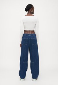 Balts garās piedurknes īsais tops savienots ar brīviem, tumši ziliem denim garajiem biksēm, kam ir elastīga josta un divas aizmugurējās kabatas.