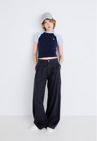 T-shirt cropped bleu marine et clair associé à un pantalon noir à taille haute et à jambes larges. Une casquette grise et des baskets blanches complètent le look.