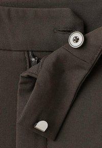 Tessuto marrone scuro con una texture diagonale, dotato di un bottone metallico e una cerniera, e un accento metallico sul ripiego del tessuto.