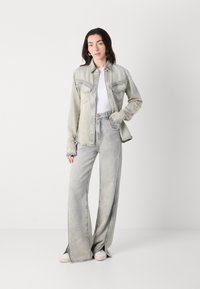 Lys grå denimjakke med to brystlommer, matchende med vide grå denimbukser med sidespalter. Stylet med en hvit topp.