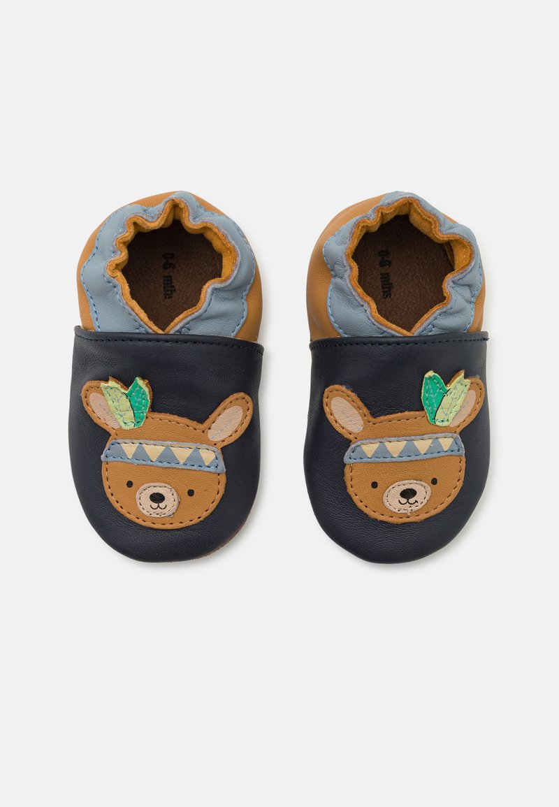 Chaussures en cuir pour bébé avec une base bleu marine, présentant un motif d'ours brun avec un bandeau bleu et des accents verts. Ouverture élastiquée pour un enfilage facile.