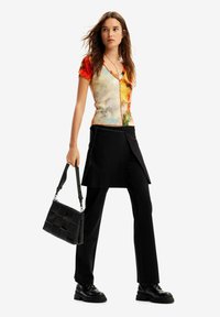 Colorful short-sleeved top with a v-neck design, paired with black trousers featuring a layered skirt overlay. Black bag with quilted pattern.