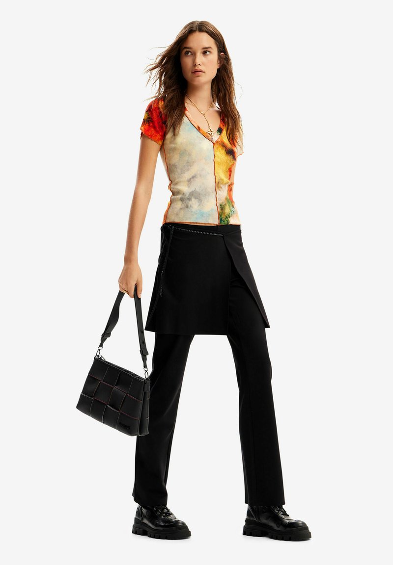 Colorful short-sleeved top with a v-neck design, paired with black trousers featuring a layered skirt overlay. Black bag with quilted pattern.