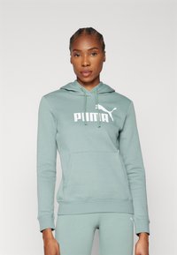 Zelená mikina s kapucňou, predným vreckom a bielym logom Puma. Mäkká tkanina, priliehavé manžety a spodný lem. Súčasť športovej sady.