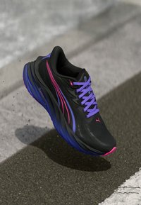 Svart treningssko med teksturert overdel, med lilla og rosa aksenter. Designet for komfort med en tykk såle og lilla snøring.