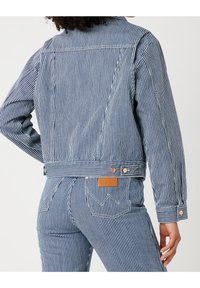 Randig denimjacka i marinblått och vitt med en kortad design, knappdetaljer och en logotyp-patch på baksidan nära midjan.