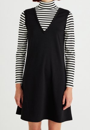 Robe noire sans manches avec un décolleté en V portée sur un col roulé ajusté rayé noir et blanc. Tissu lisse avec une coupe décontractée et un ourlet évasé.