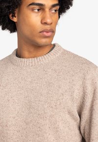 Lichtbeige gebreide trui met een geribbelde ronde halslijn, textuurstof en spikkels. Geen zichtbare logo's of versieringen.