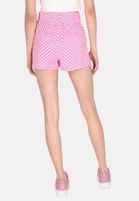Shorts a quadretti rosa e bianchi con elastico in vita. I pantaloni sono sopra il ginocchio, abbinati a scarpe rosa.