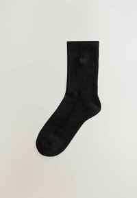 Sorte ribbede sokker lavet af blødt materiale, med en afrundet tå og et præget "self" logo nær toppen.