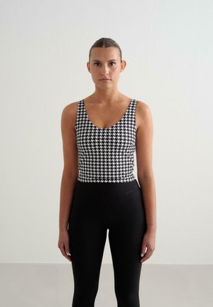 Czarna i biała top z wzorem houndstooth, z szerokimi ramiączkami, zestawiony z dopasowanymi czarnymi legginsami z gładkim pasem.