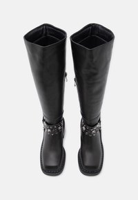 Μαύρες μπότες μέχρι το γόνατο από λείο δέρμα, με τετραγωνική μύτη, διακοσμητική ταινία με τρουκς και πλαϊνούς φερμουάρ για εύκολη εφαρμογή.