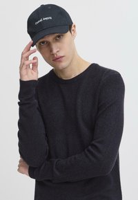 Căciulă neagră cu cuvântul "Casual" în litere albe; pulover închis la culoare cu guler rotund și manșete ribbate; textură fină, design minimalist.