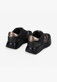 Las zapatillas deportivas negras presentan una textura suave con detalles en bronce metálico y un talón texturizado. La suela es negra y ligeramente elevada.
