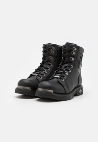 Bottines en cuir noir avec œillets en métal, lacets texturés, bout rond et accents de logo argenté sur le bout et sur le côté. Semelle robuste.