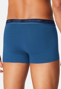 Male wearing blue patterned boxer briefs with a navy waistband labeled "uncover," shown from the back at mid-thigh level.
