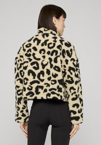 Falscher Pelzjacke mit beigefarbenem Grundton und schwarzem Leopardenmuster. Verfügt über einen hohen Kragen und einen kurzen Schnitt. Strukturierte, weiche Fellstruktur.