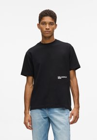 Fekete pamut grafikai póló, kerek nyakkivágással és rövid ujjal, elől fehér "KARL LAGERFELD JEANS" logóval.